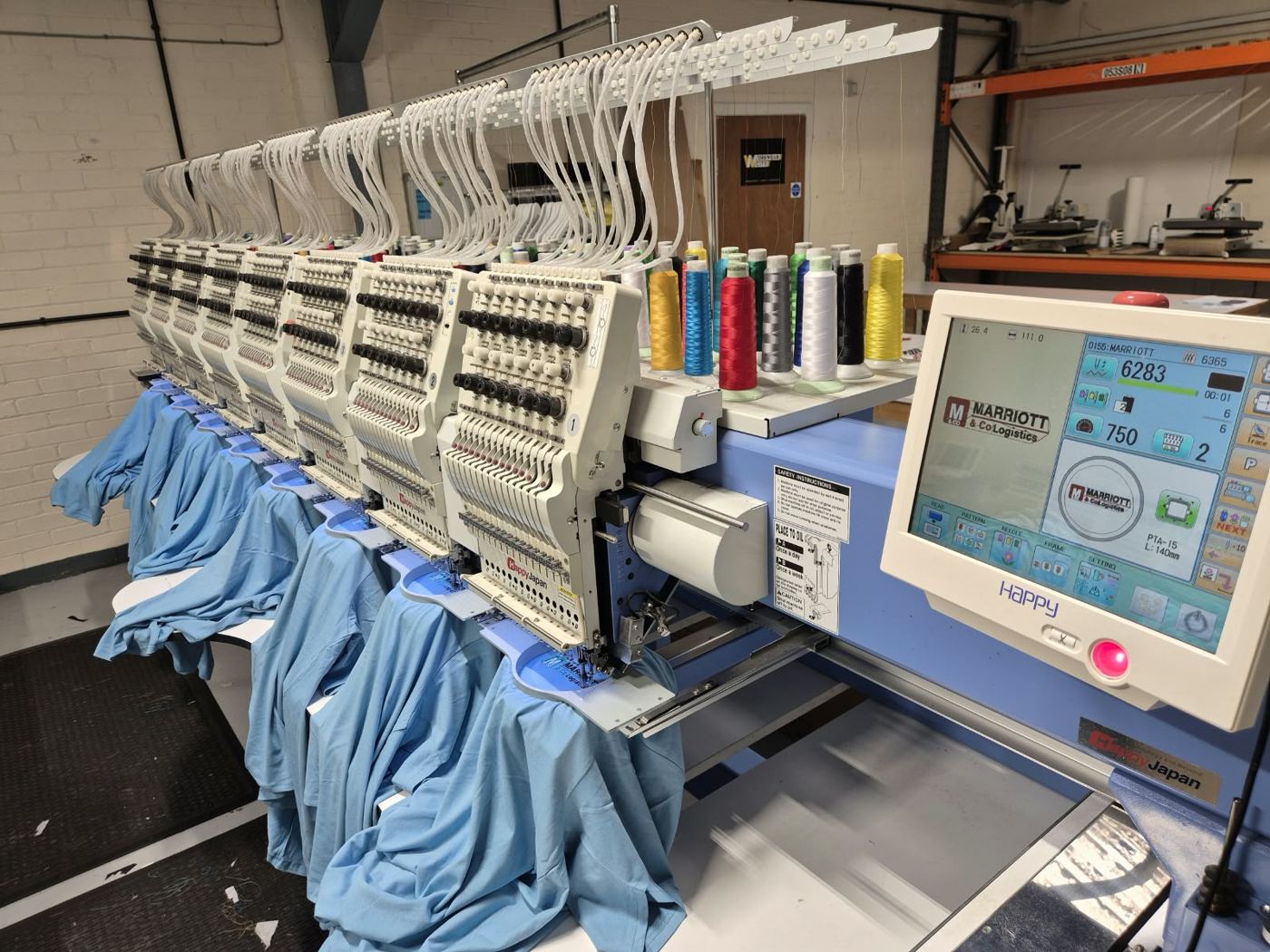 Multi head embroidery machines stitching blue shirts in the Stitches 2 Impress studio
